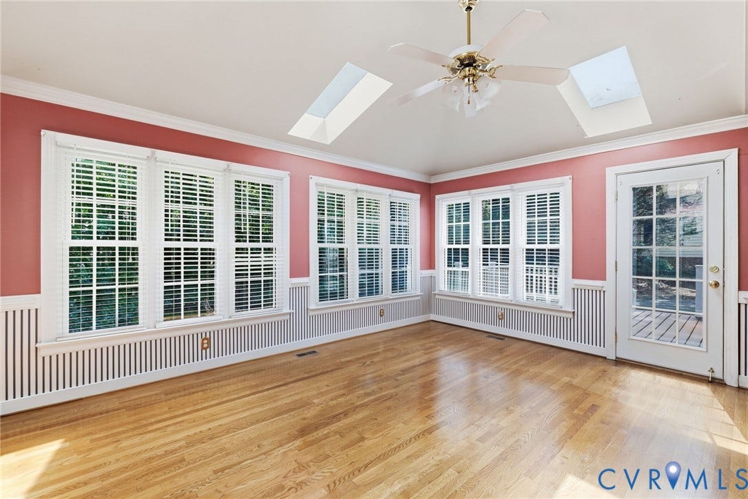 Hardwood flooring with a ceiling fan, multiple windows with blinds, a skylight, and a glass-paneled door
