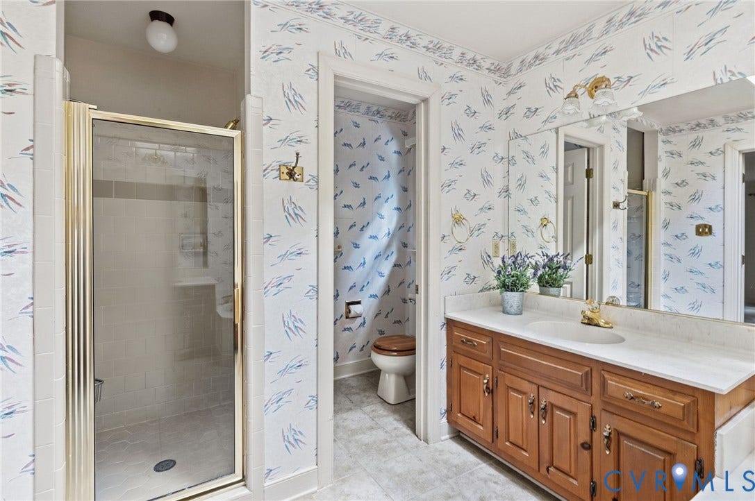 Double vanity with a white countertop and integrated sinks, wood-finish cabinetry, and a glass-enclosed shower with tiled walls