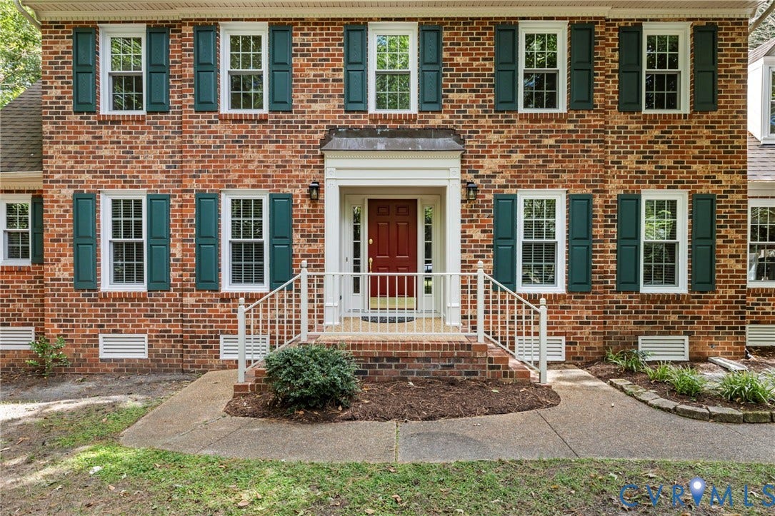 Brick exterior with green window shutters, white-trimmed windows, and a red front door