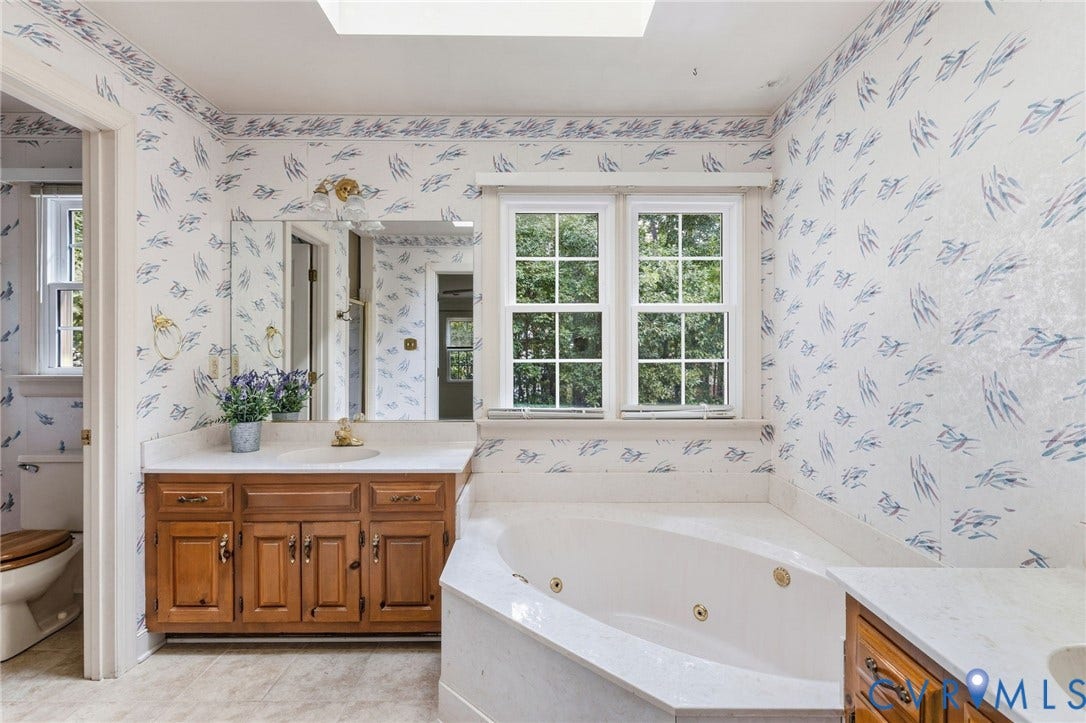 Bathroom featuring a corner jetted tub, a vanity with a white countertop and wood-finish cabinetry, a skylight, and dual windows