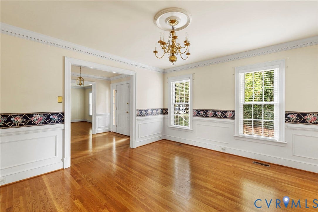 Hardwood flooring throughout, two large windows with blinds, detailed crown molding, wainscoting, and a chandelier with ceiling medallion