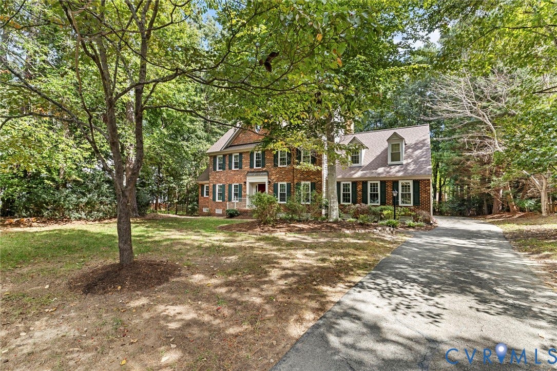 Traditional brick exterior with green shutters, dormer windows, a paved driveway, and mature trees