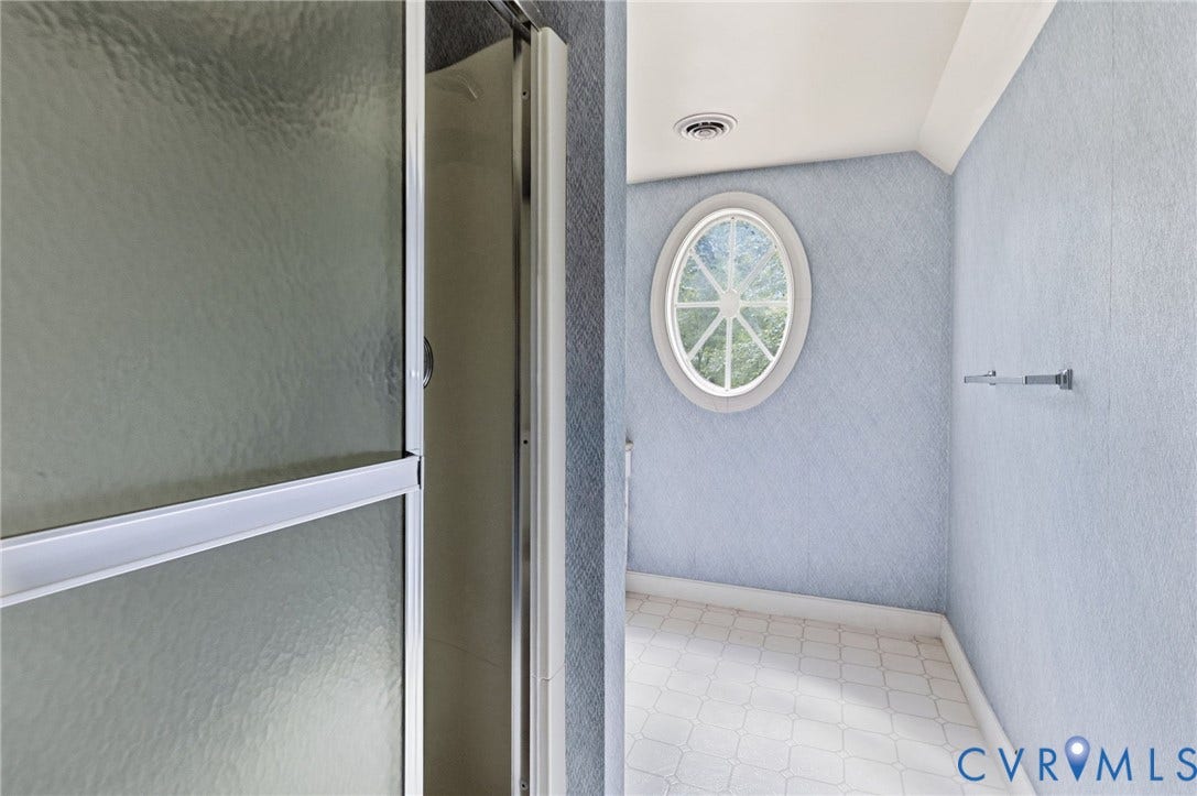 Frosted glass shower enclosure, oval window, tile flooring, and wall-mounted towel bar