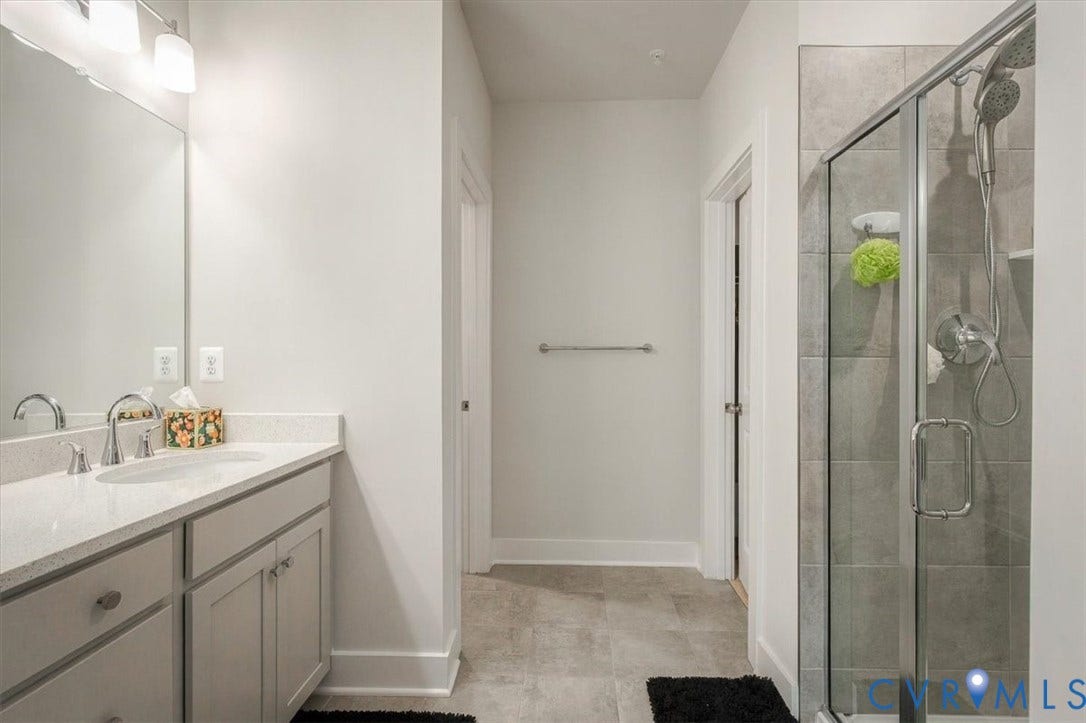 9690 Turning Point Dr, #A, 4E300, Glen Allen, VA 23059 Dual-sink vanity with a light-toned countertop, large mirrored wall, glass-enclosed shower, and tiled flooring