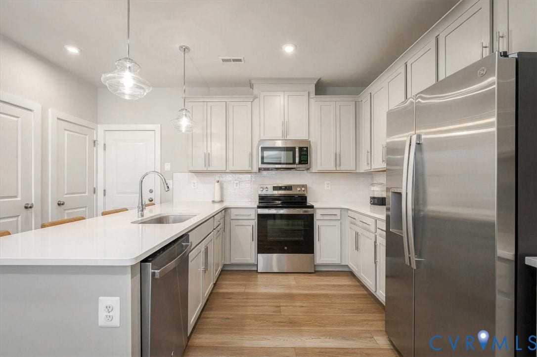 9690 Turning Point Dr, #A, 4E300, Glen Allen, VA 23059 Modern kitchen featuring white shaker-style cabinetry, stainless steel appliances, white quartz countertops with waterfall edge detailing at the island, pendant lighting, and warm wood-finish flooring throughout