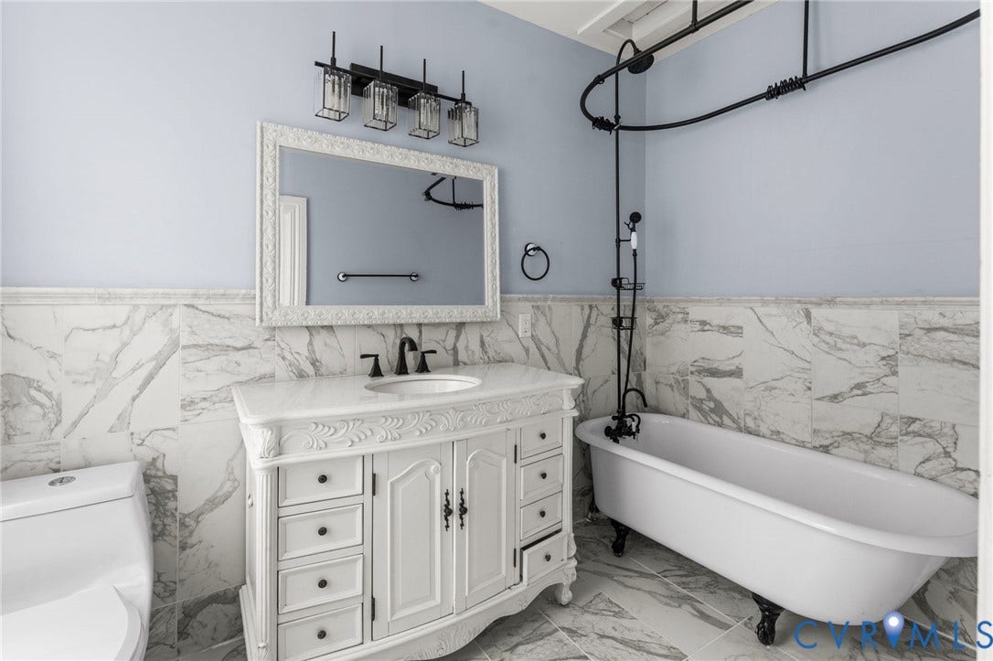 724 N 1st Street, Jackson Ward, Richmond, VA 23219 White clawfoot bathtub with a black shower system, white carved vanity with an undermount sink, and a decorative framed mirror