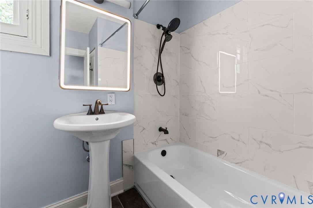 724 N 1st Street, Jackson Ward, Richmond, VA 23219 Pedestal sink with bronze-finish faucet, illuminated mirror, and tiled tub/shower combination with matte black fixtures