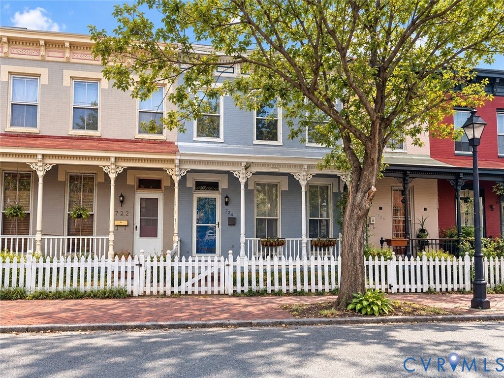724 N 1st Street, Jackson Ward, Richmond, VA 23219 Architectural row house facade featuring a white picket fence, a covered front porch, decorative porch columns, and a brick sidewalk