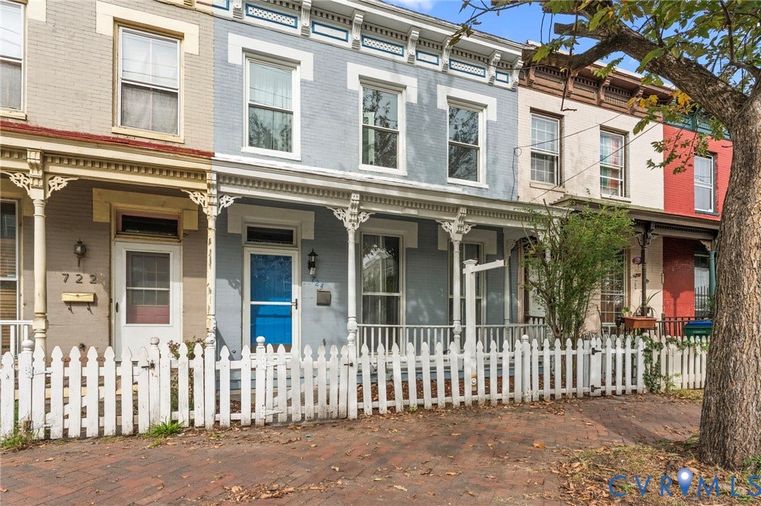 724 N 1st Street, Jackson Ward, Richmond, VA 23219 Brick facade row home featuring a white picket fence, covered front porch, and decorative porch columns