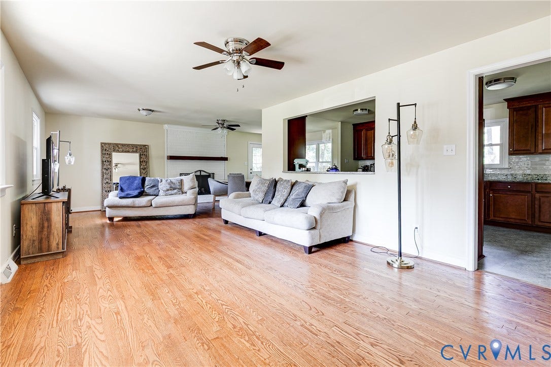 Expansive living area featuring wood-finish flooring, a ceiling fan, and a pass-through window to the kitchen