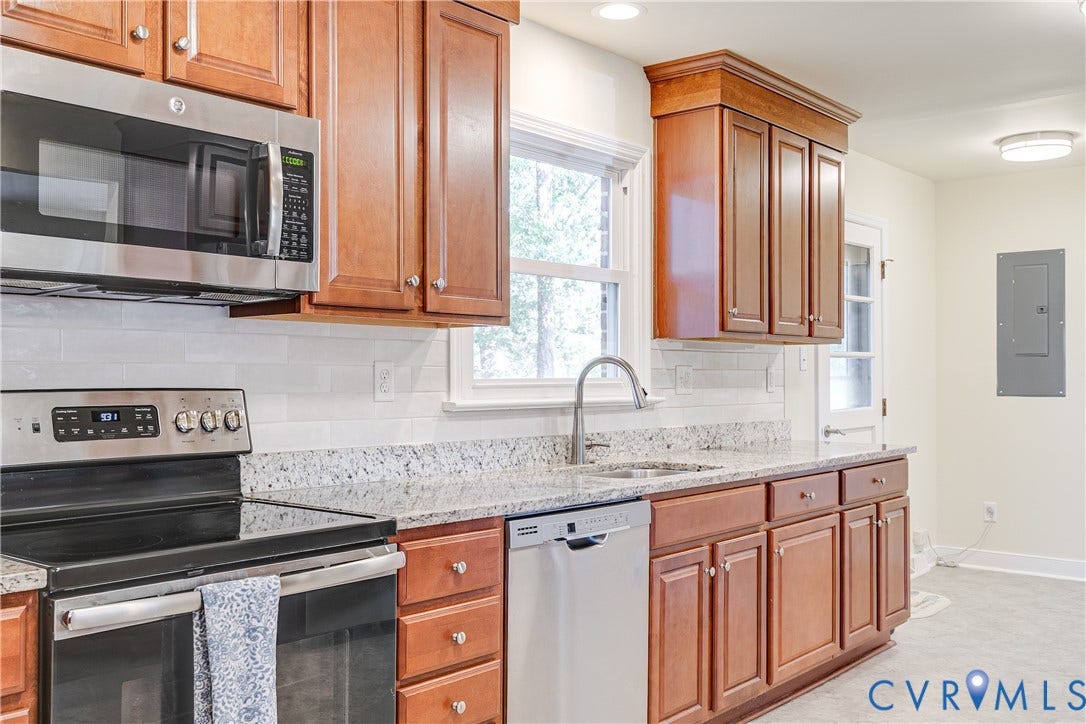 Stainless steel appliances, wood-finish cabinetry, granite countertops, subway tile backsplash, and recessed lighting