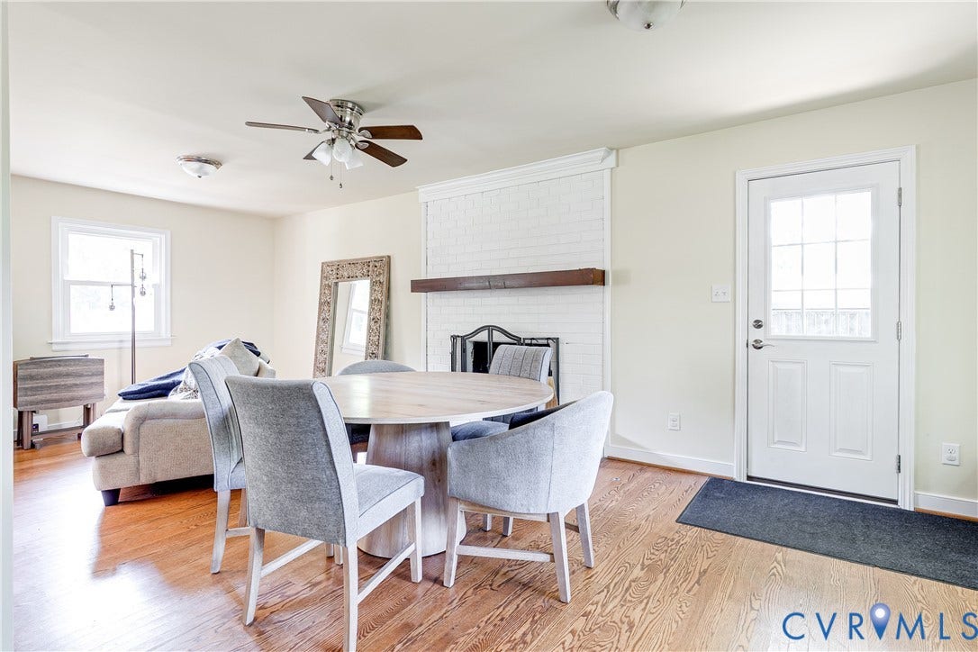 Hardwood flooring, painted brick fireplace with wood mantel, ceiling fan, white paneled door with glass insert, and a double-hung window