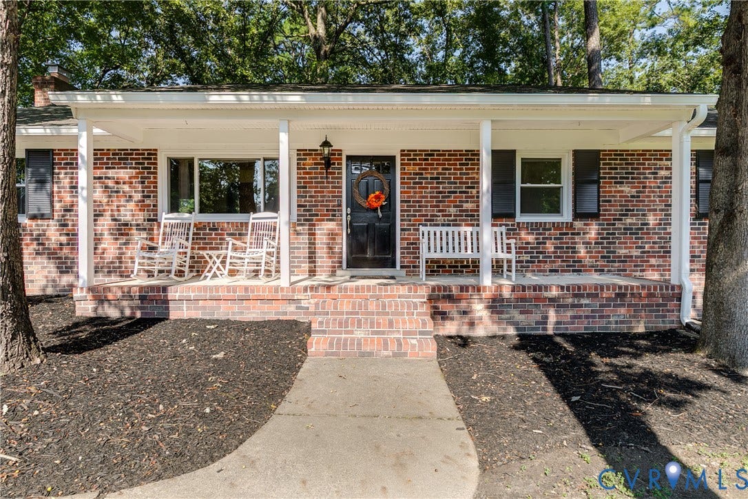 Brick exterior featuring a covered porch with white columns, concrete pathway, and mature trees