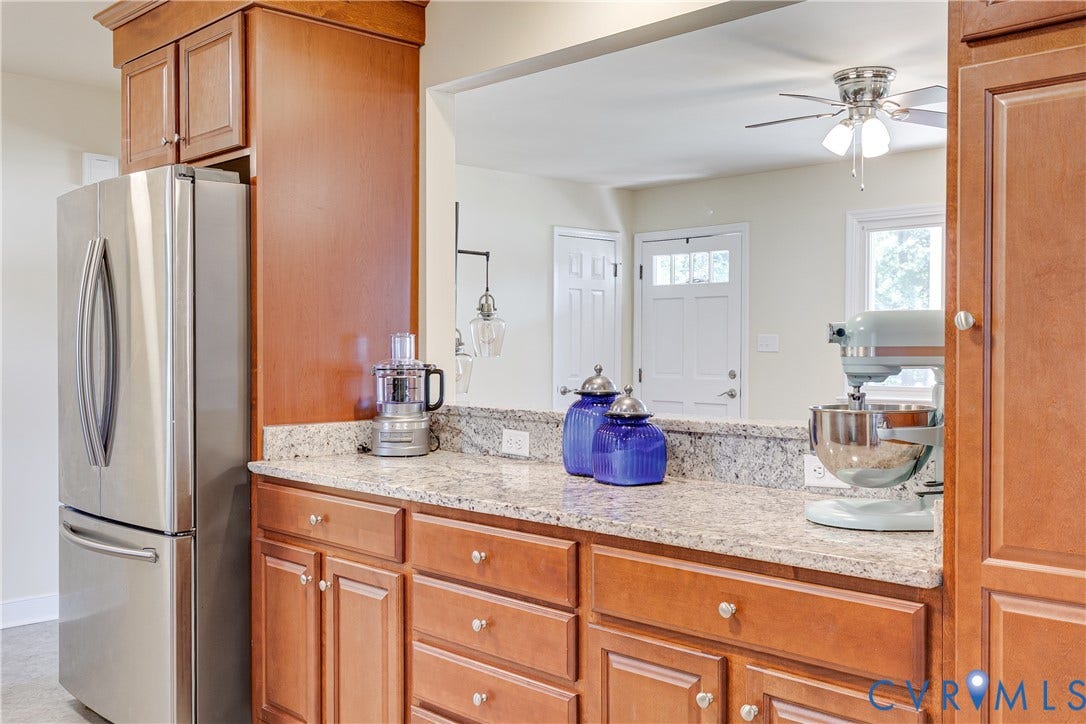 Stainless steel refrigerator, wood-finish cabinetry, light-toned countertops, and a built-in ceiling fan