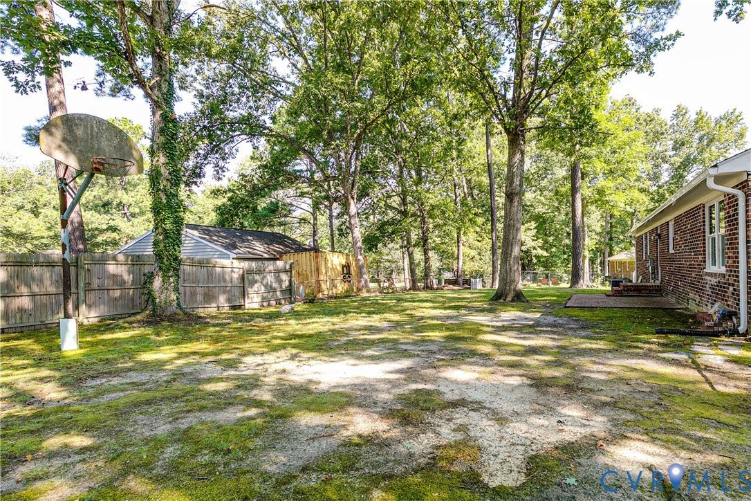 Expansive backyard featuring mature trees, a wooden privacy fence, brick exterior, and a paved patio