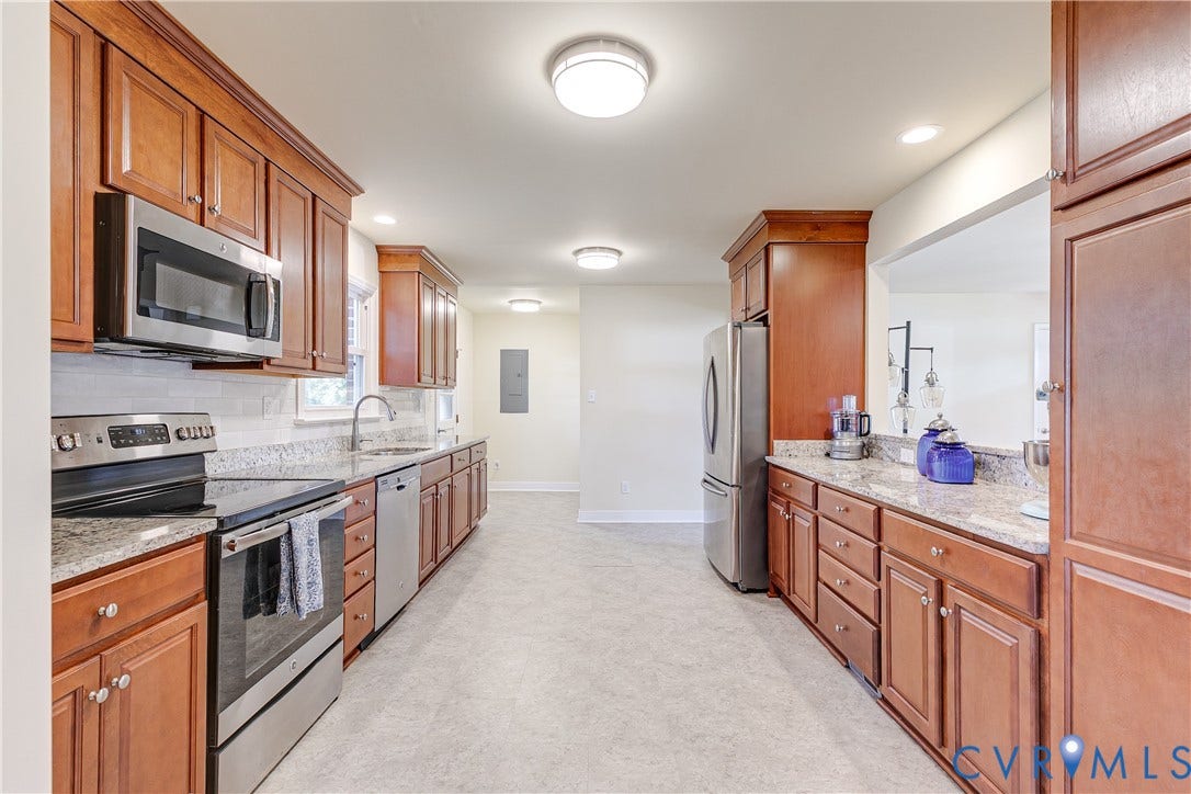 Full-height wood-finish cabinetry, stainless steel appliances, speckled countertops, and a subway tile backsplash