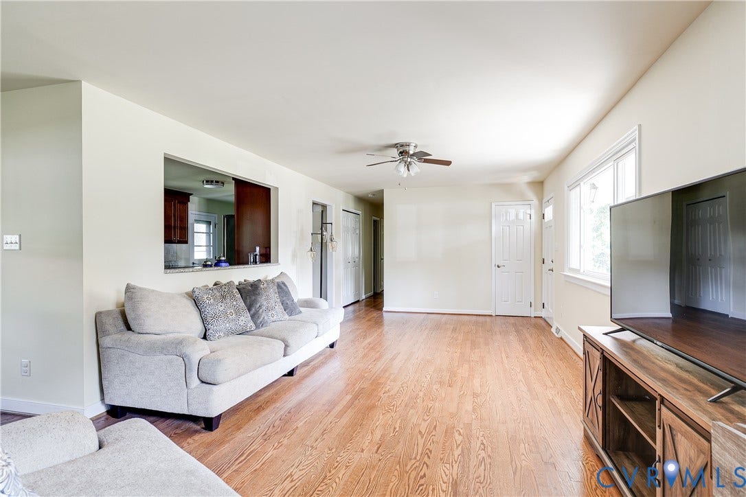 Wood-finish flooring, recessed kitchen pass-through, ceiling fan, white paneled doors, and bright window