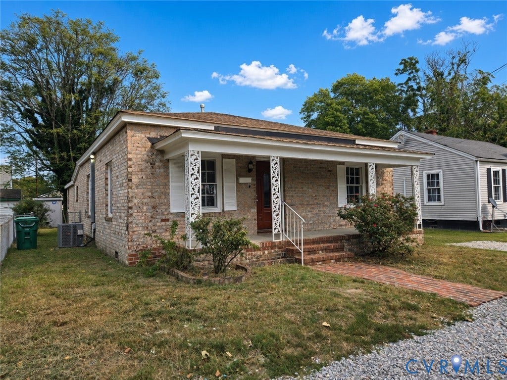 1223 Paul Street, Hillcrest, Petersburg, VA 23803 Brick exterior with a covered front porch featuring decorative white columns, a brick pathway, and a gravel driveway