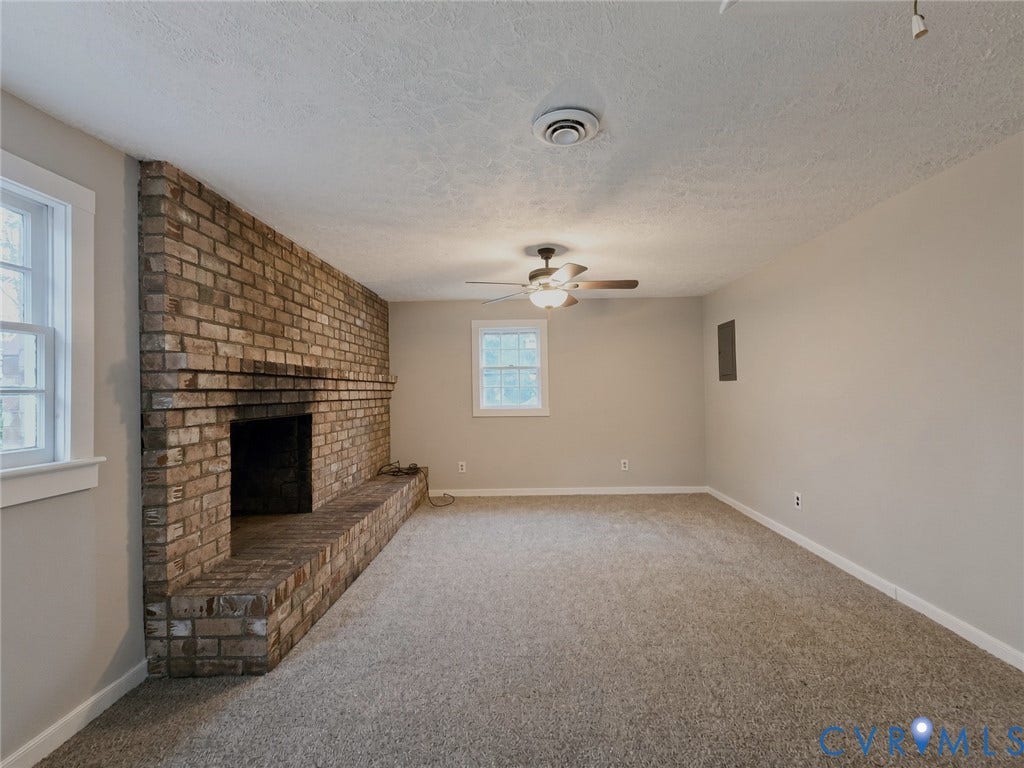 1223 Paul Street, Hillcrest, Petersburg, VA 23803 Expansive brick fireplace with a raised hearth, light-toned carpeting, neutral wall paint, and a ceiling fan with integrated lighting