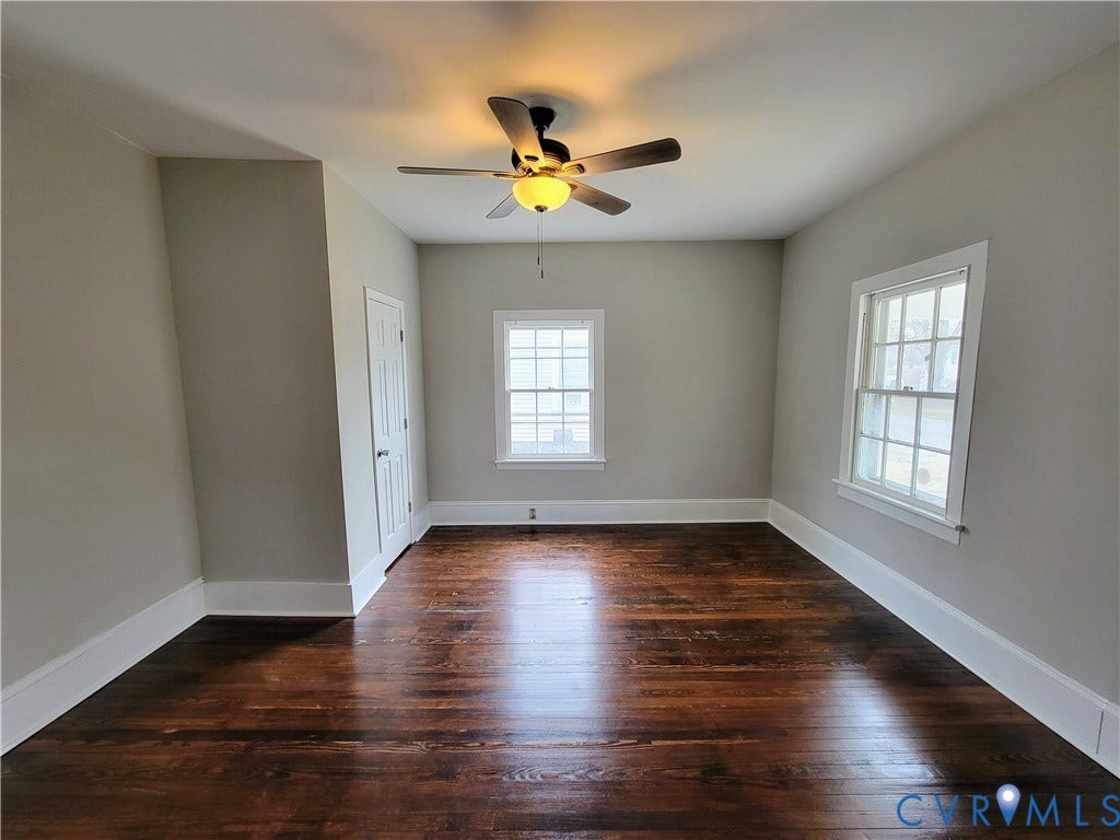 1223 Paul Street, Hillcrest, Petersburg, VA 23803 Bright, light-filled room featuring hardwood flooring, ceiling fan with integrated lighting, dual windows with white trim, and clean white walls