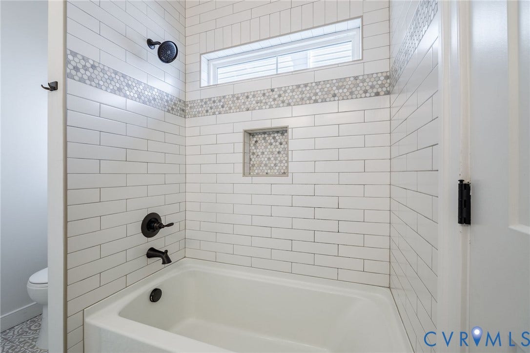 2902 Lawson Street, Richmond, VA 23224 White subway tile surround with decorative hexagonal mosaic accent tile, matte black shower fixtures, built-in tiled niche, and transom window