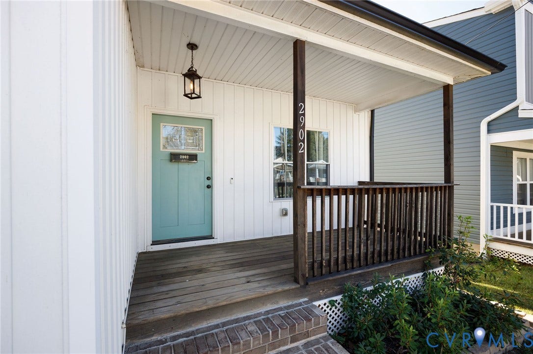 2902 Lawson Street, Richmond, VA 23224 Covered front porch with wood decking, vertical board-and-batten siding, dark wood railing, brick-stepped entrance, and a decorative paneled door