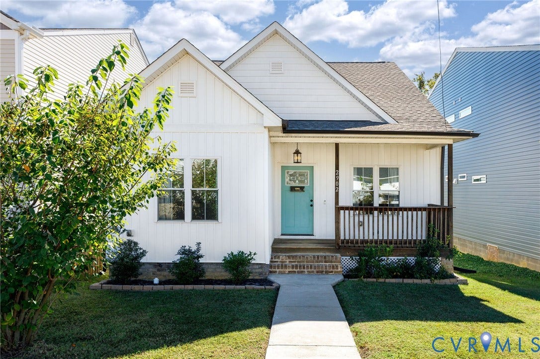 2902 Lawson Street, Richmond, VA 23224 Single-story residence featuring white vertical siding, a covered front porch with a dark wood-finish railing, a brick-accented entryway, and a solid-color front door