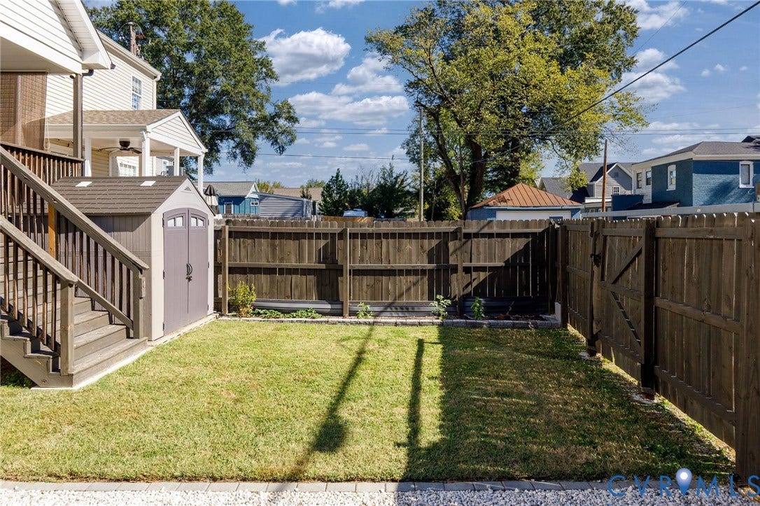 2902 Lawson Street, Richmond, VA 23224 Fenced backyard featuring a manicured lawn, raised stone-bordered garden bed, and a resin storage shed