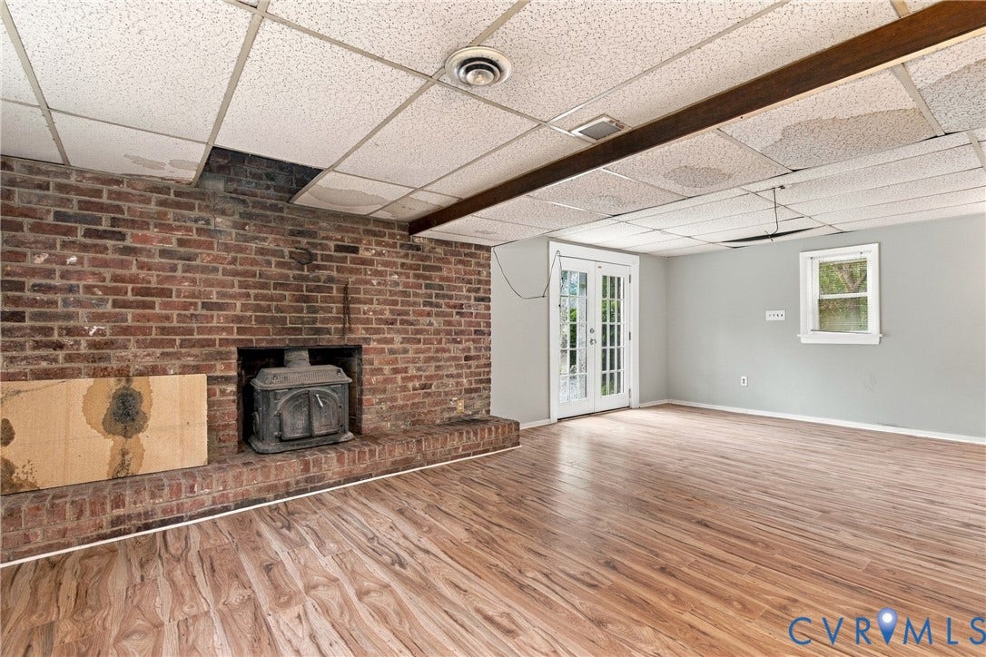 8150 Bradbury Road, Henrico, VA 23231 LVP flooring, brick fireplace with a cast iron stove, double French doors, and a single-pane window