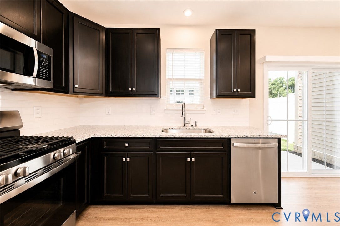 10607 Pink Lilly Lane, Chester, VA 23831 Dark wood-finish cabinetry with silver hardware, light-toned countertop, stainless steel appliances, white subway tile backsplash, and wood-finish flooring