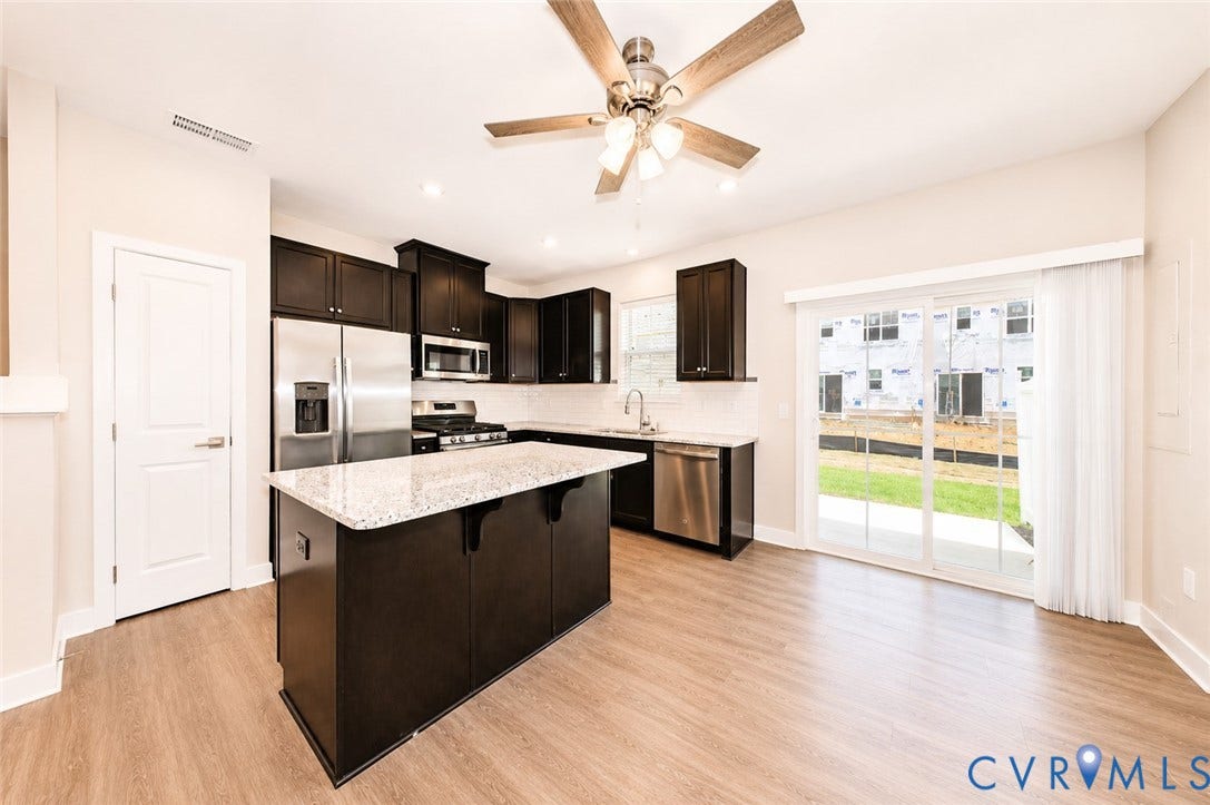 10607 Pink Lilly Lane, Chester, VA 23831 Kitchen featuring wood-finish flooring, dark cabinetry, stainless steel appliances, a center island with a light-colored countertop, and a sliding glass door to the exterior