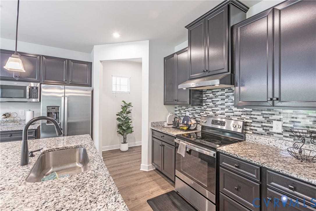 1943 Enon Station Drive, Chester, VA 23836 Kitchen featuring stainless steel appliances, dark cabinetry, light granite countertops, a stainless steel sink with a matte black faucet, and a mosaic tile backsplash