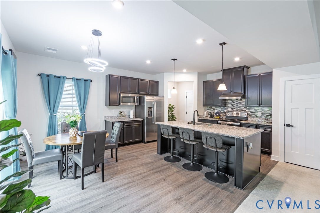 1943 Enon Station Drive, Chester, VA 23836 Open-concept kitchen and dining area featuring wood-finish flooring, dark wood cabinetry, stainless steel appliances, and a kitchen island with seating