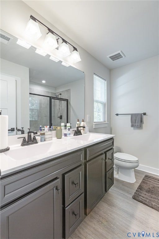 1943 Enon Station Drive, Chester, VA 23836 Dual vanity with dark cabinetry and white countertops, large mirror, shower with dark-framed glass enclosure, and wood-finish flooring