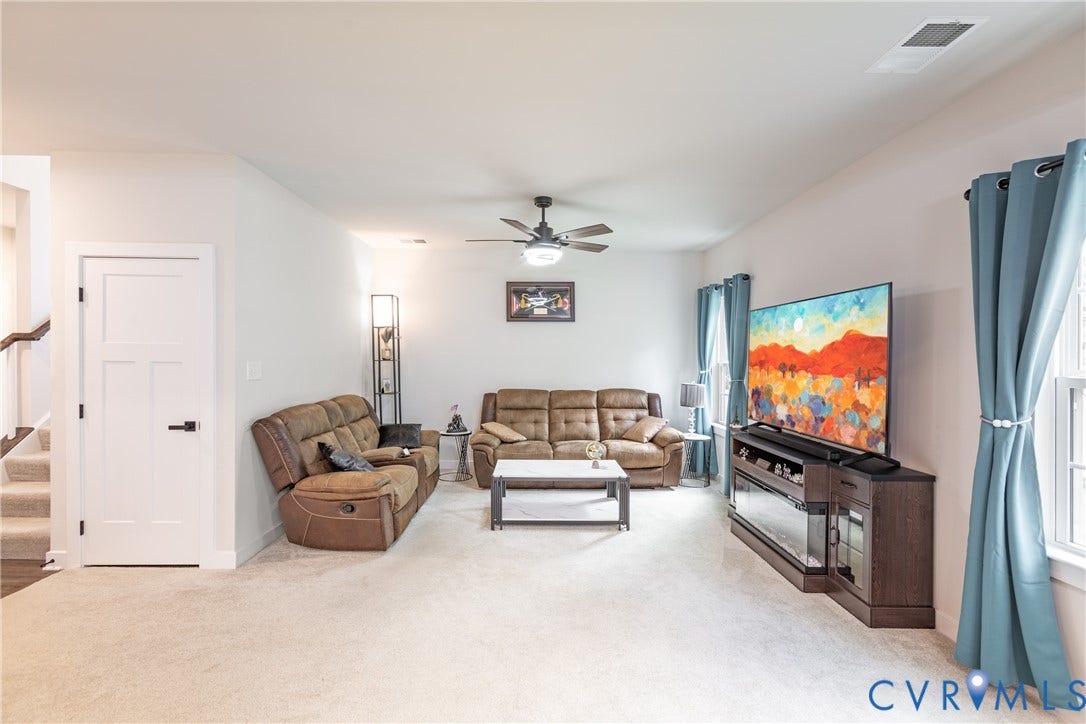 1943 Enon Station Drive, Chester, VA 23836 Spacious living area featuring light-colored carpeting, a ceiling fan with integrated lighting, and multiple windows