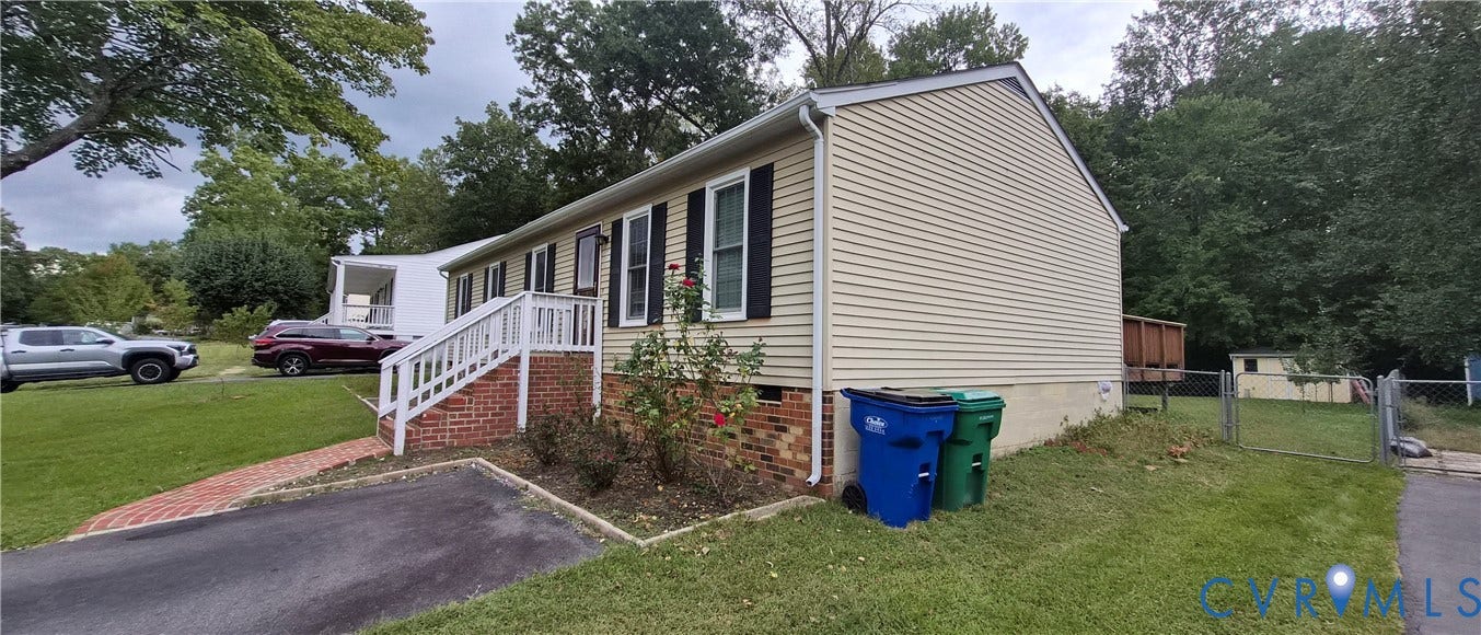 Siding exterior with brick foundation, white handrails, and mature trees