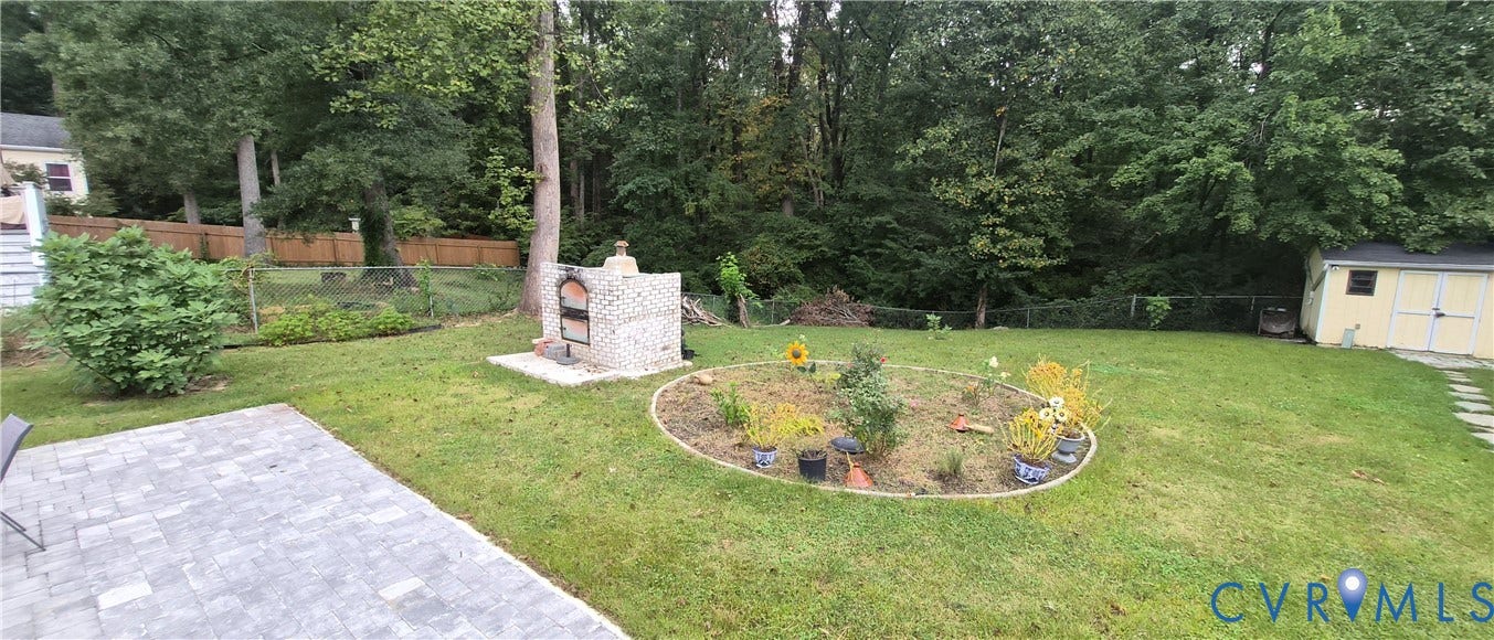 Expansive backyard featuring a paver patio, built-in brick oven, circular planting bed, and a storage shed