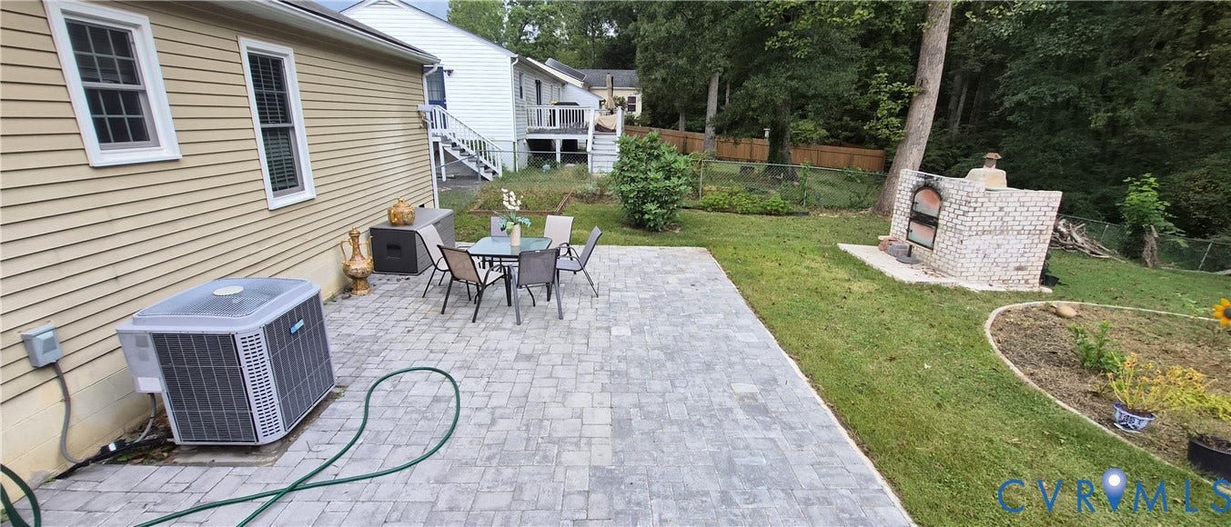 Expansive paver patio with a built-in outdoor pizza oven, surrounded by a manicured lawn and mature trees