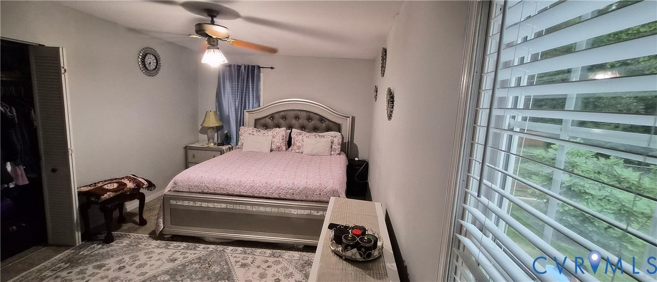 Bedroom featuring a ceiling fan with light fixture, window with horizontal blinds, and a built-in closet with bifold doors