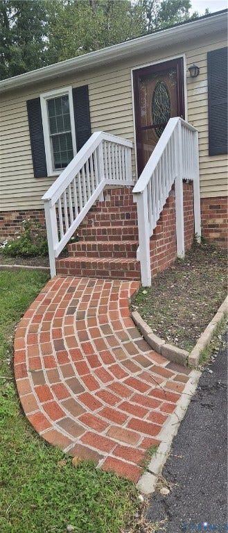 Brick walkway leading to a brick staircase with white railings, featuring a decorative glass storm door and exterior wall siding
