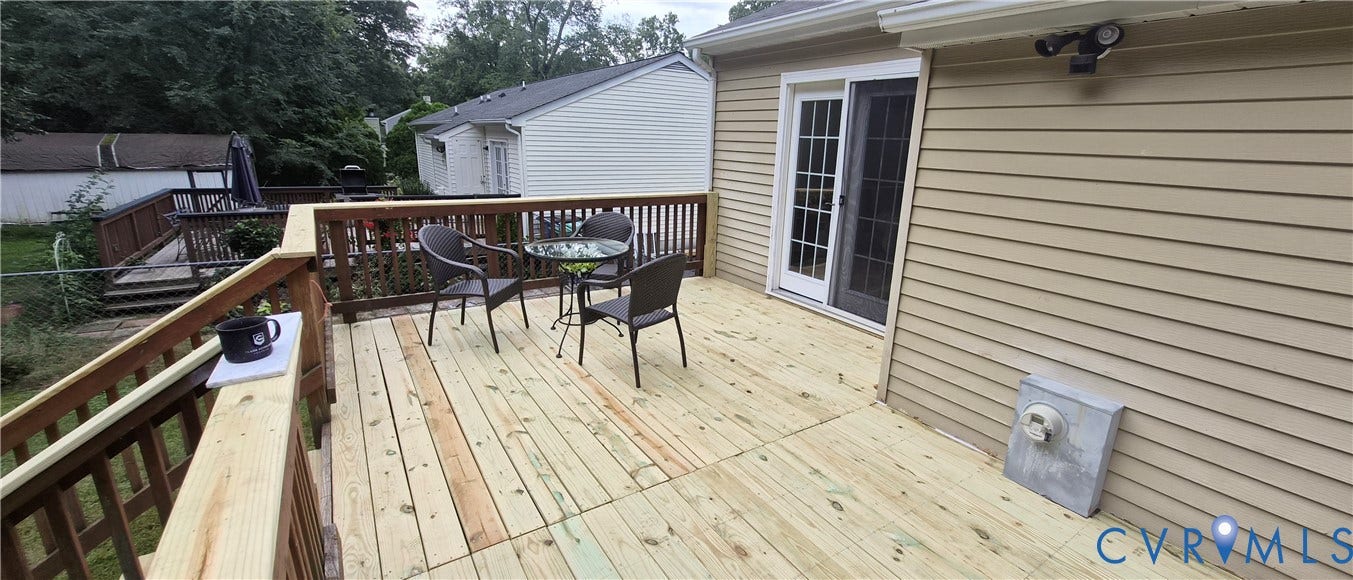 Expansive wood deck with a full railing system, directly accessible via a sliding glass door, featuring light-colored horizontal siding