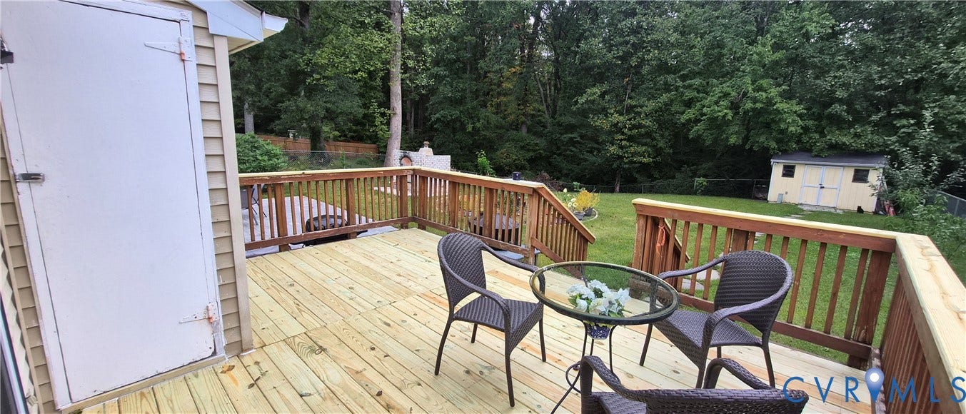 Expansive wood deck with natural wood railing, overlooking a green lawn with mature trees and a detached shed