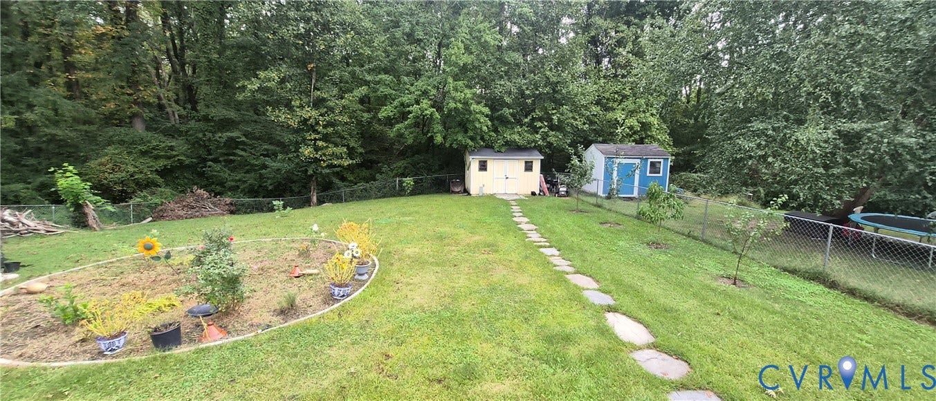 Expansive lawn area with a stone pathway, two storage sheds, and a wire fence
