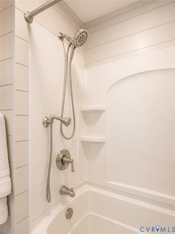 White tub and shower combination with brushed nickel fixtures, built-in shelving, and shiplap-style wall paneling