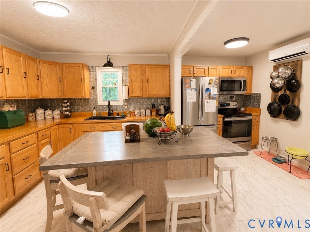 Kitchen featuring wood cabinetry, stainless steel appliances, a large center island with seating, a window above the sink, and light-toned flooring