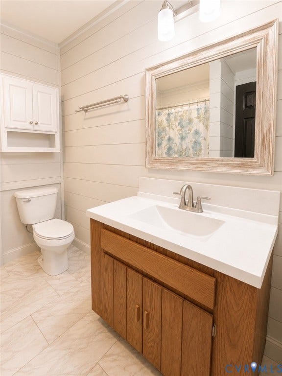 White shiplap walls, wood-finish vanity with white countertop and integrated sink, white tile flooring, and wall-mounted storage cabinetry