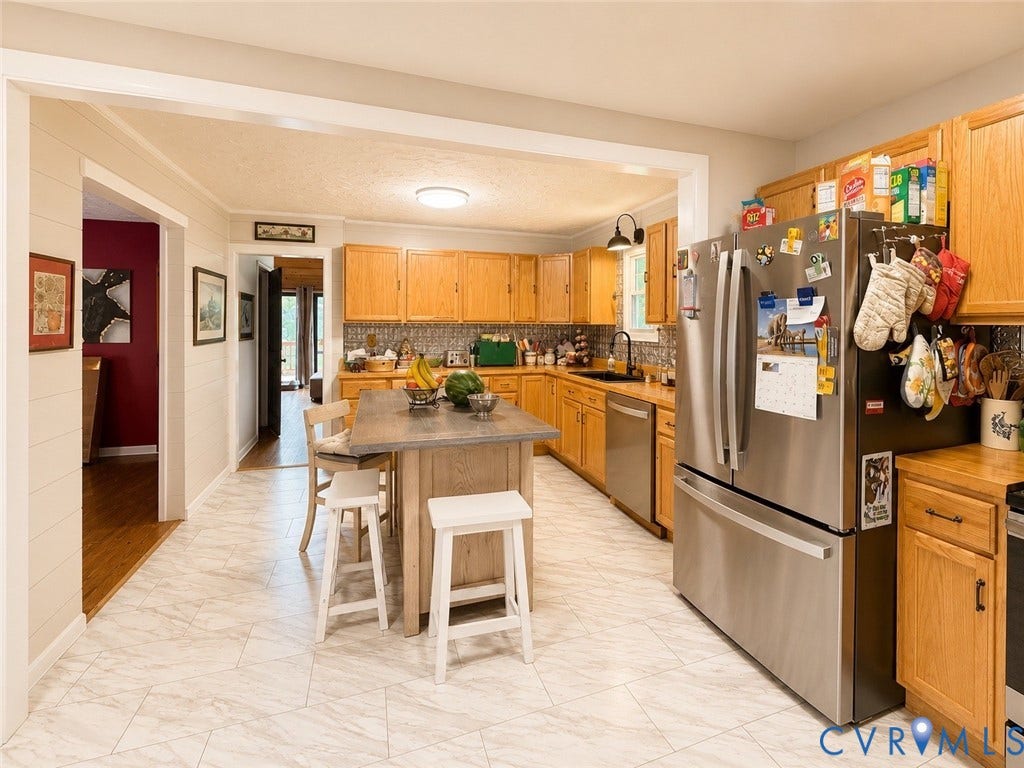 Kitchen featuring wood cabinetry, stainless steel appliances, a center island with seating, patterned tile flooring, and a decorative tile backsplash