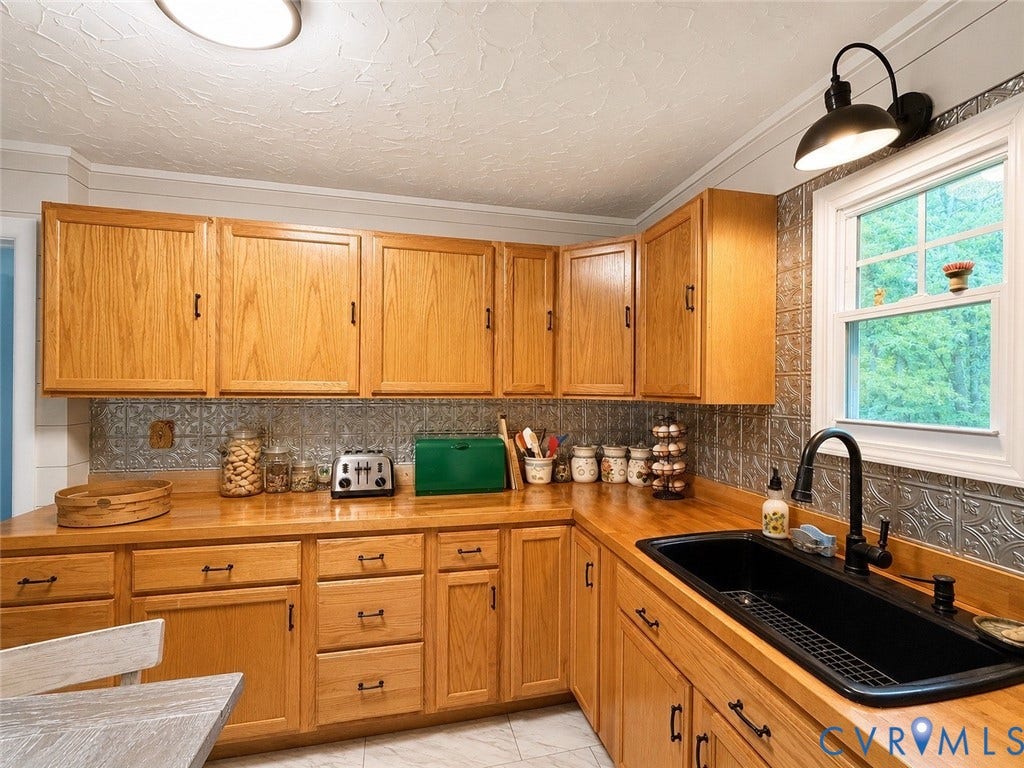 Wood cabinetry with black hardware, wood-finish countertops, black single-basin sink, black wall-mounted faucet, and textured backsplash