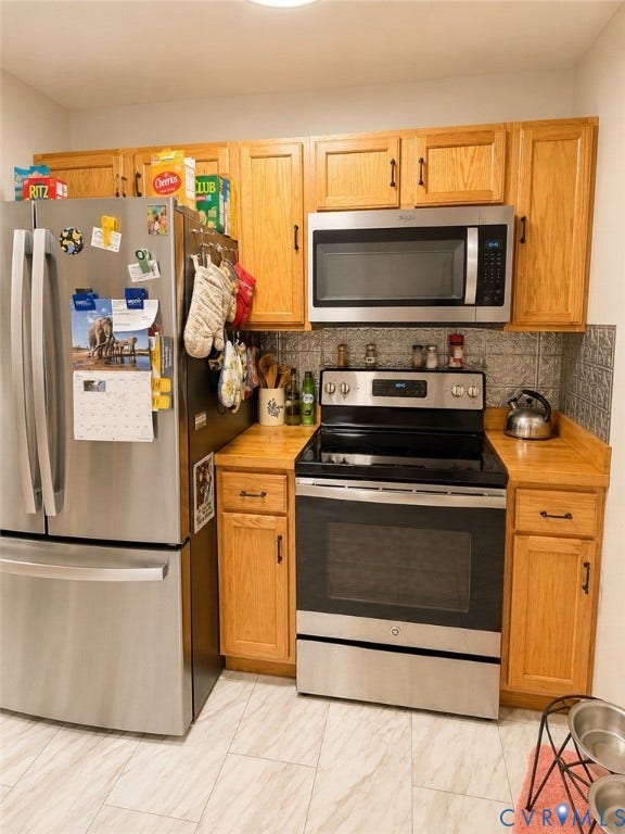 Stainless steel refrigerator and range, wood-finish cabinetry, patterned backsplash, wood-finish countertops, and light-toned tile flooring