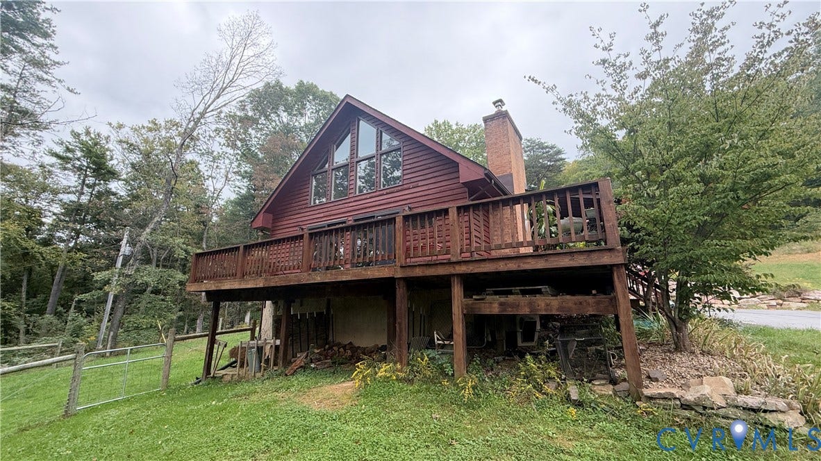 A-frame architecture with a prominent brick chimney, elevated wood deck, large triangular windows, and wooded surroundings